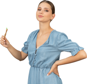 Vista di tre quarti di una giovane donna orgogliosa in abito blu che tiene in mano uno spazzolino da denti