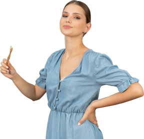 Three-quarter view of a proud young woman in blue dress holding a toothbrush