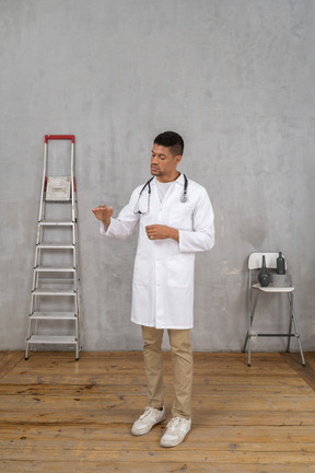 Three-quarter view of a young doctor standing in a room with ladder and chair showing a size of something