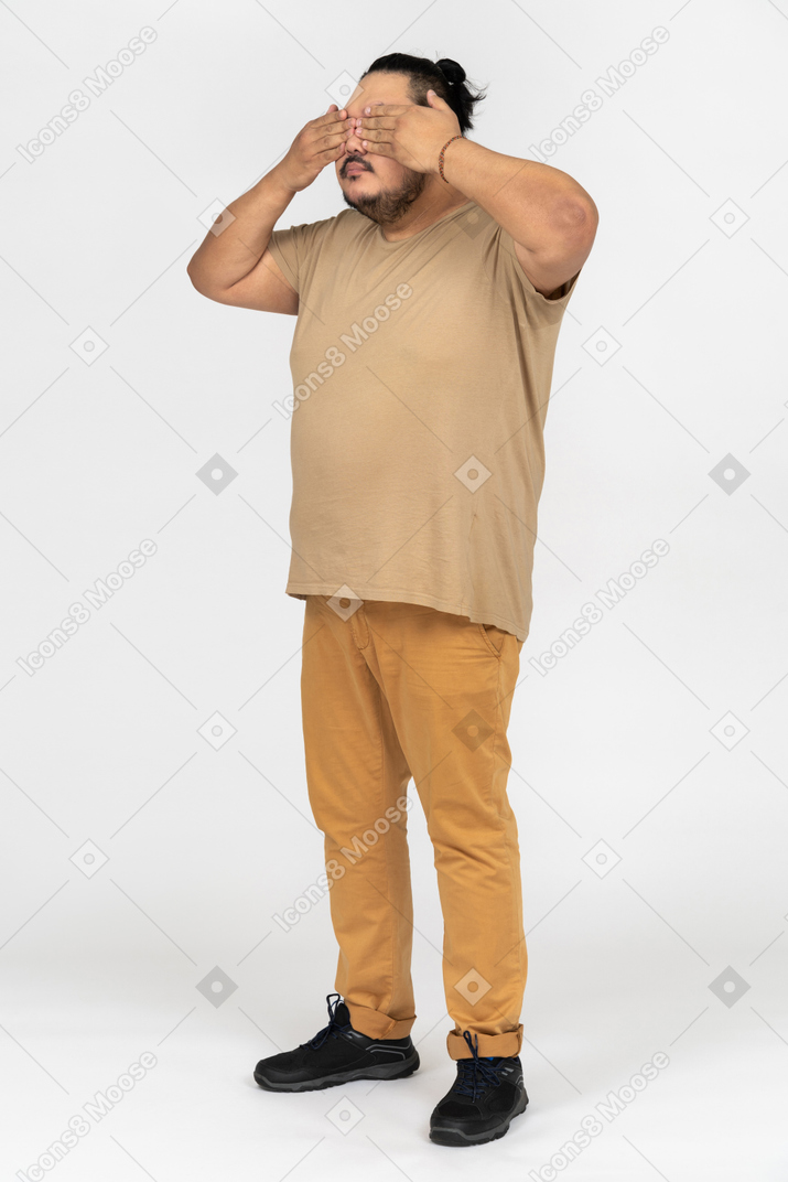 Plump asian man covering his eyes with both hands