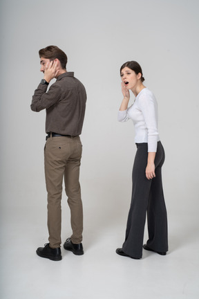 Vue de trois quarts arrière d'un jeune couple en tenue de bureau écoutant les rumeurs