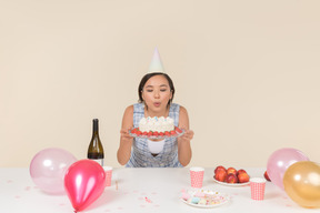 Joven asiática soplando velas en el pastel de cumpleaños