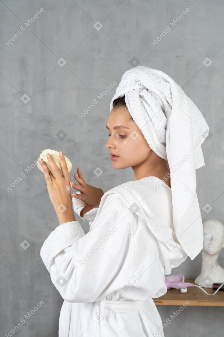 Vista laterale di una donna in accappatoio che applica crema per le mani