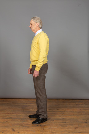 Vista lateral de um velho descontente vestindo um pulôver amarelo e fechando os olhos
