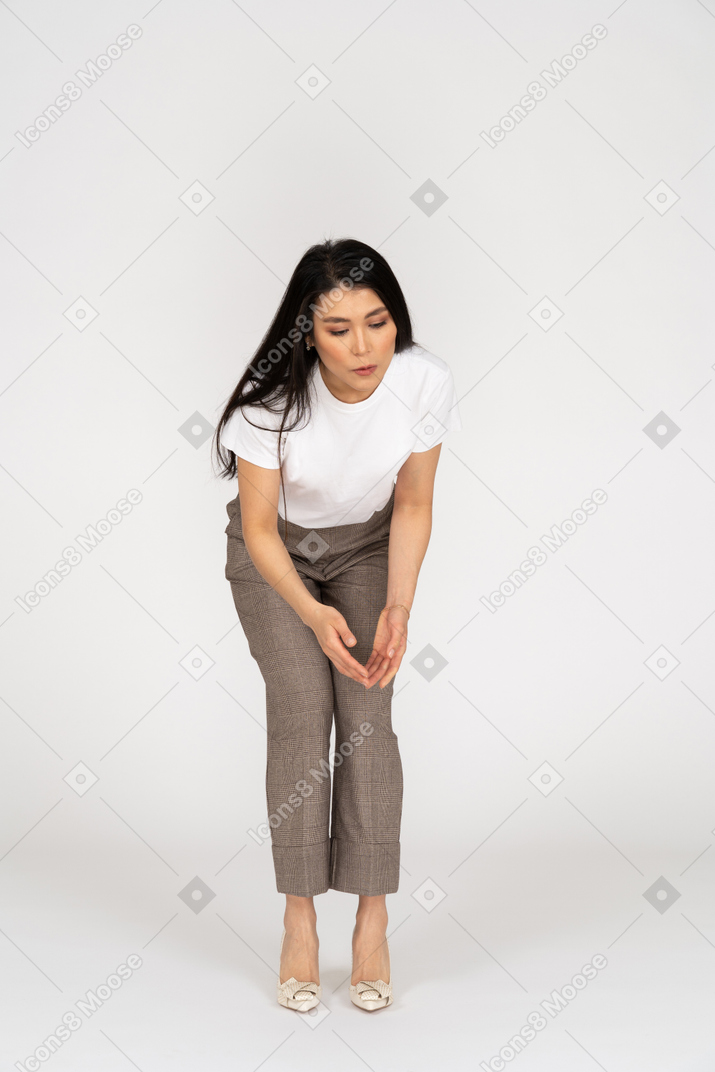 Front view of a questioning young lady in breeches and t-shirt raising hands and bending down