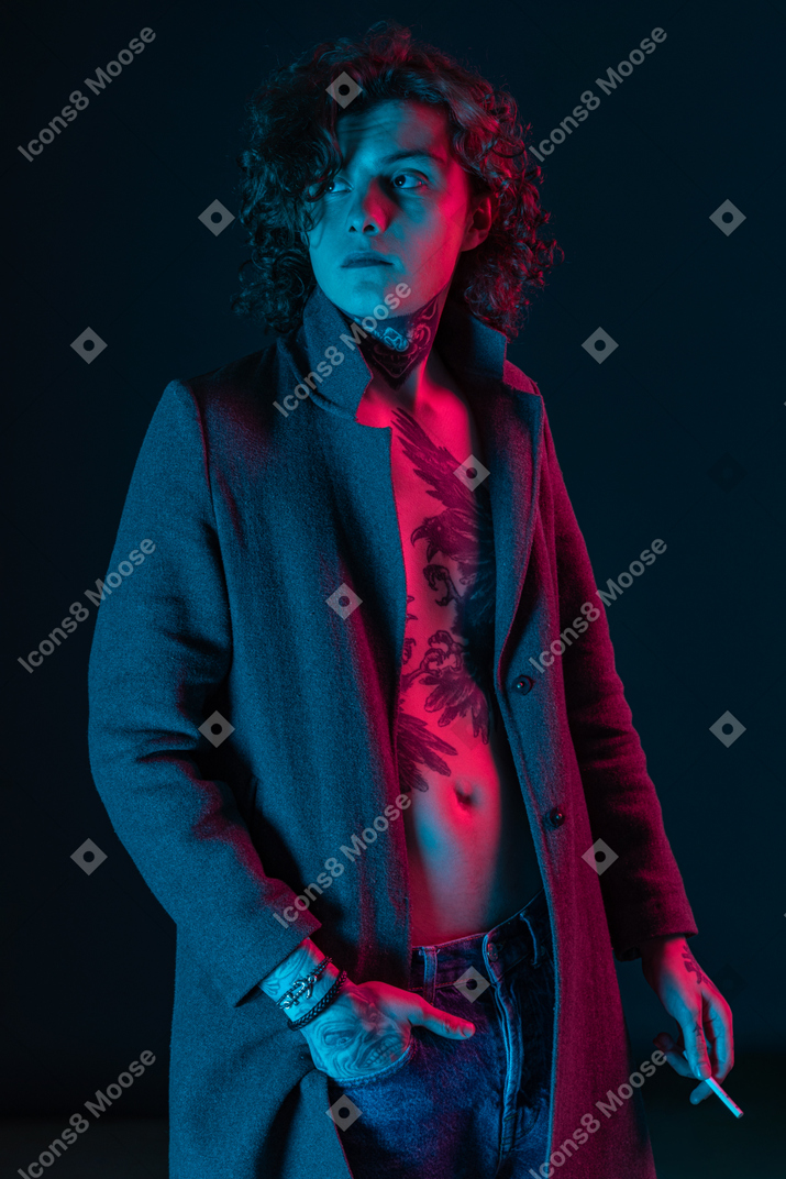 Молодой взрослый мужчина держит сигарету в темноте