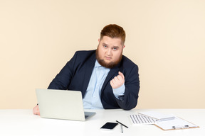 Junger übergewichtiger büroangestellter, der mit geballter faust am schreibtisch sitzt