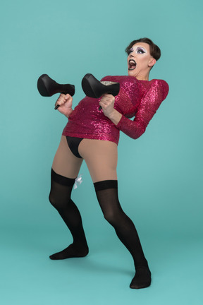 Portrait of a drag queen armed with a pair of high-heel shoes pretending to shoot