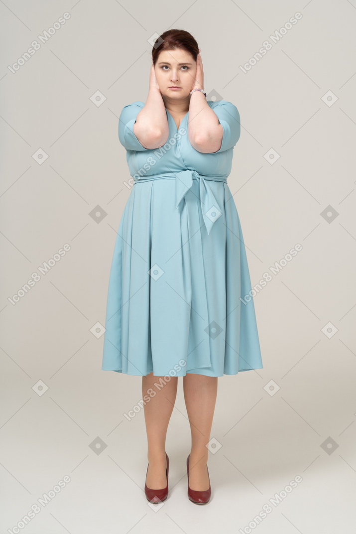Front view of a woman in blue dress covering ears with hands