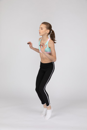 Three-quarter view of a teen girl in sportswear raising hands while standing on tiptoes