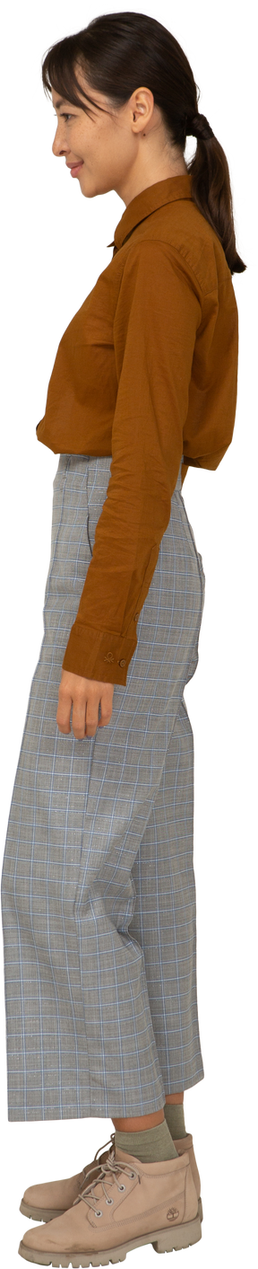 Vista lateral de uma jovem mulher asiática sorridente de calça e blusa