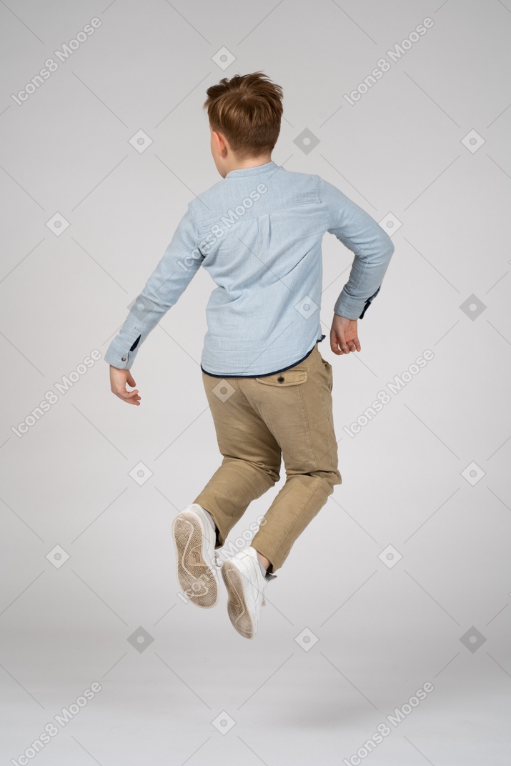 Back view of a boy in blue shirt jumping high in the air