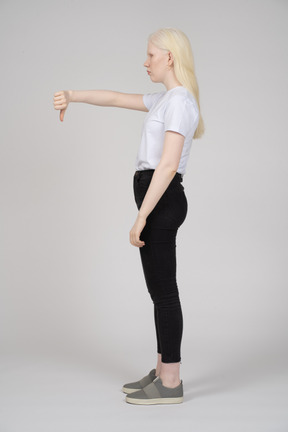 Vista lateral de uma jovem loira em pé com os polegares para baixo