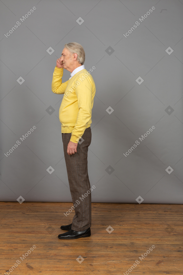 一个困惑的老人摸头，穿着一件黄色的套衫的侧视图