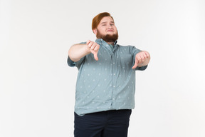 Junger übergewichtiger mann, der daumen unten mit beiden händen zeigt