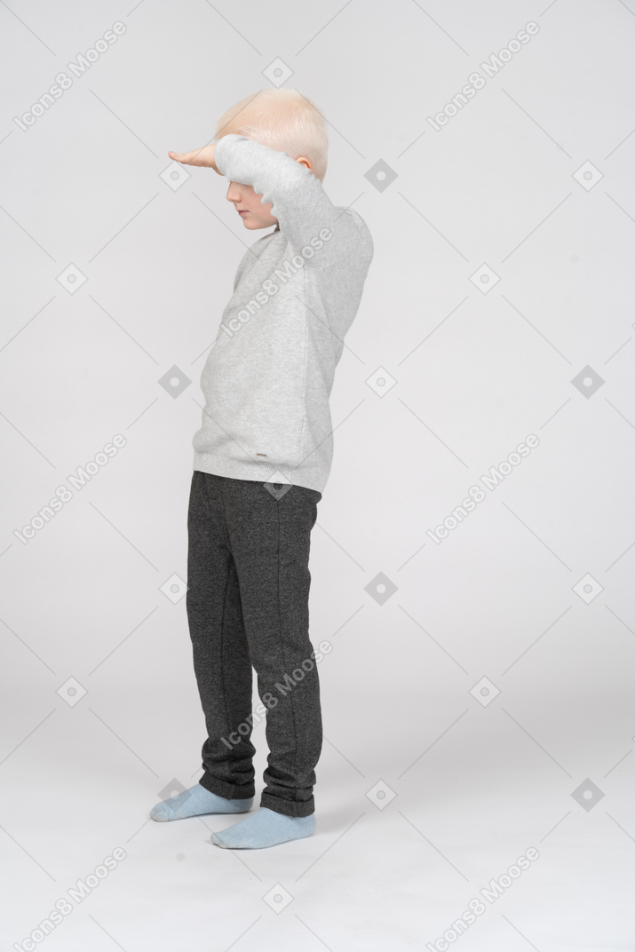 一个男孩用手放在额头上看东西的侧视图