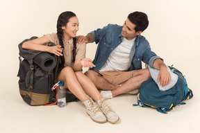 Jovem casal interracial sentado perto de mochilas e falando