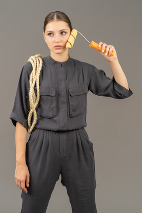 Woman in gray coveralls holding a paint roller to her cheek