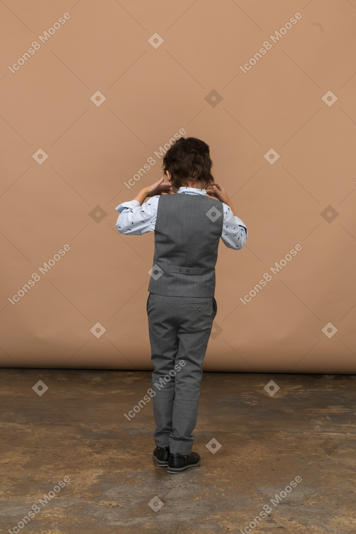 Vista trasera de un niño con traje tocando las orejas