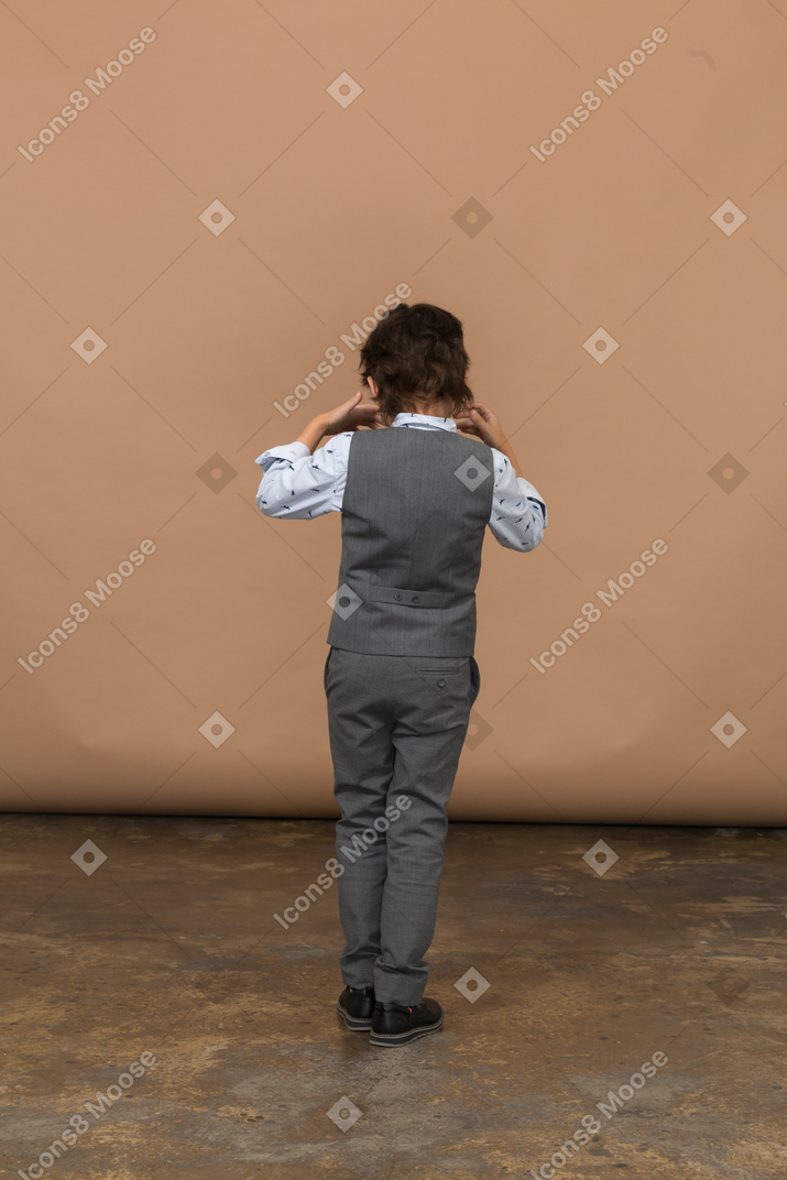 Rear view of a boy in suit touching ears