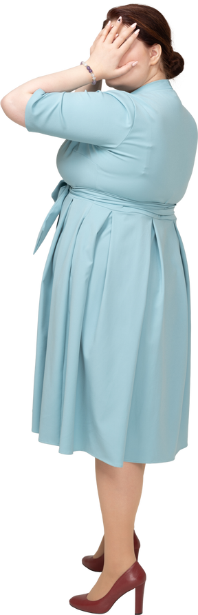 一个穿着蓝色连衣裙的女人用手遮住眼睛的侧视图