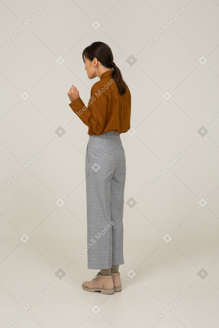 Three-quarter back view of a young gesticulating asian female in breeches and blouse
