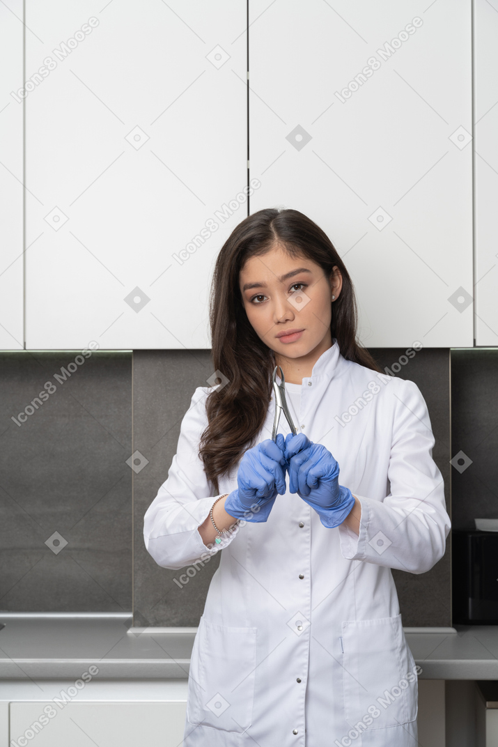 Front view of thoughtful female doctor holding dental instrument and looking at camera