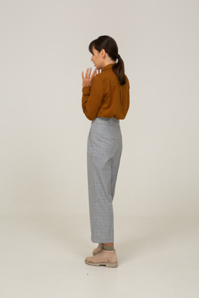 Vista traseira a três quartos de uma jovem mulher asiática de calça e blusa, levantando as mãos