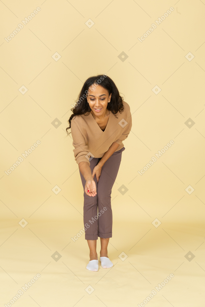 弯下腰，伸出一只手的皮肤黝黑的年轻女性的前视图