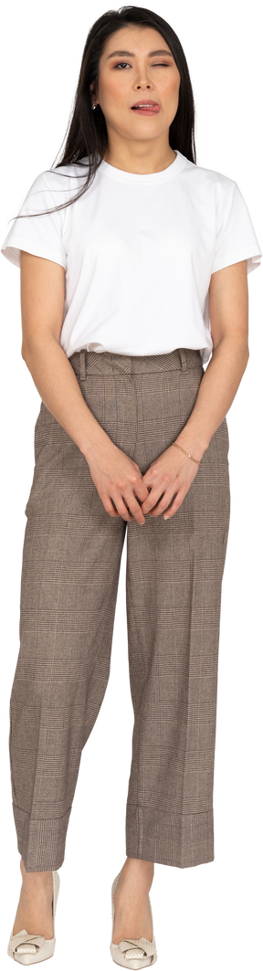 Vista frontale di una giovane donna ammiccante in calzoni e maglietta che mostra la lingua