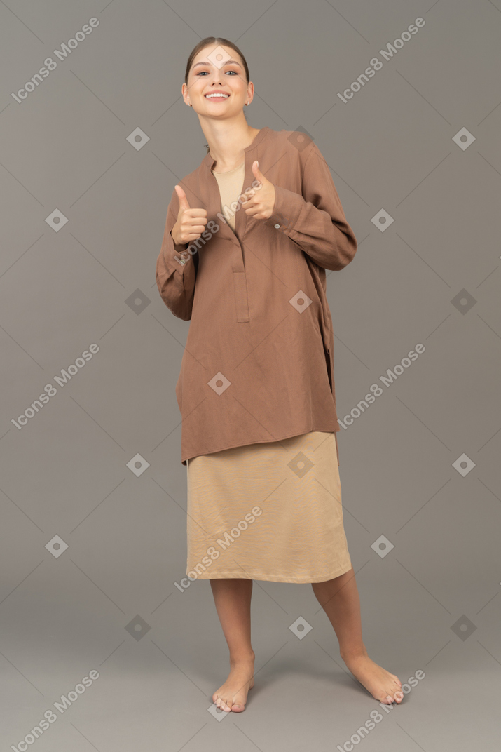 Young barefoot woman flashing two hands with thumbs up while looking at camera