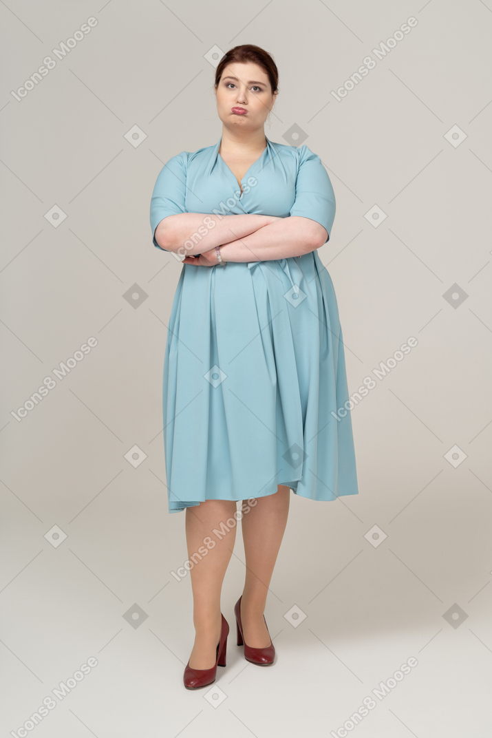Front view of a woman in blue dress standing with crossed arms