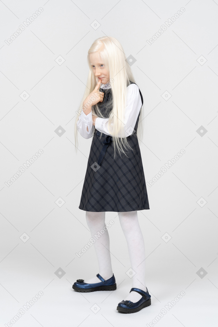Schoolgirl smiling mischievously with finger pressed to mouth