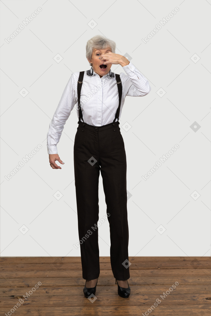 Front view of an old female in office clothes sneezing indoors