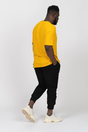 黄色のtシャツを着て歩いている若い浅黒い肌の男の4分の3の背面図