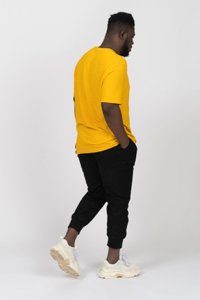 Three-quarter back view of a walking young dark-skinned man in yellow t-shirt