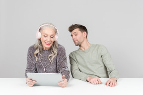 Пожилая женщина в наушниках и молодой парень смотрят что-то на цифровом планшете