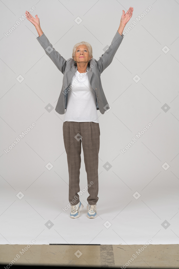 一位身着西装的老太太站在脚趾上举起双臂的前视图