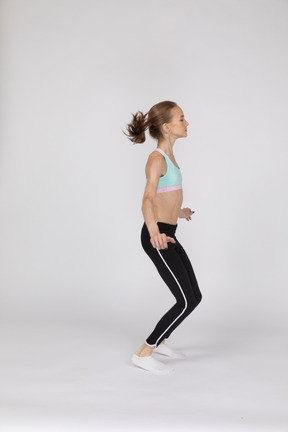 Side view of a teen girl in sportswear squatting and putting hands on hips