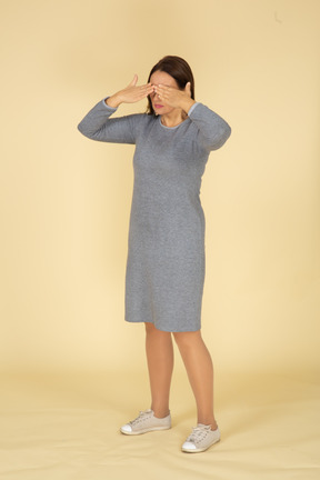Vista lateral de uma mulher de vestido cinza fechando os olhos com as mãos