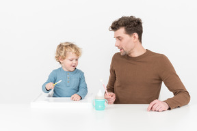 赤ちゃんの息子にスプーンの使い方を教える父親