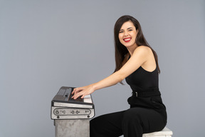 Side view of a smiling sitting young lady in black suit while playing the piano