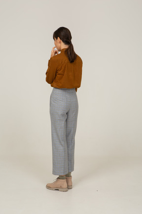 Three-quarter back view of a young asian female in breeches and blouse touching mouth