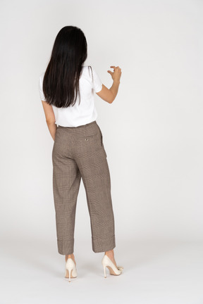 Vista traseira de três quartos de uma jovem de calça e camiseta branca mostrando o tamanho de alguma coisa