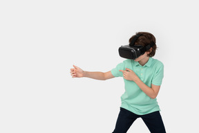 Menino com fone de ouvido de realidade virtual segurando arma invisível