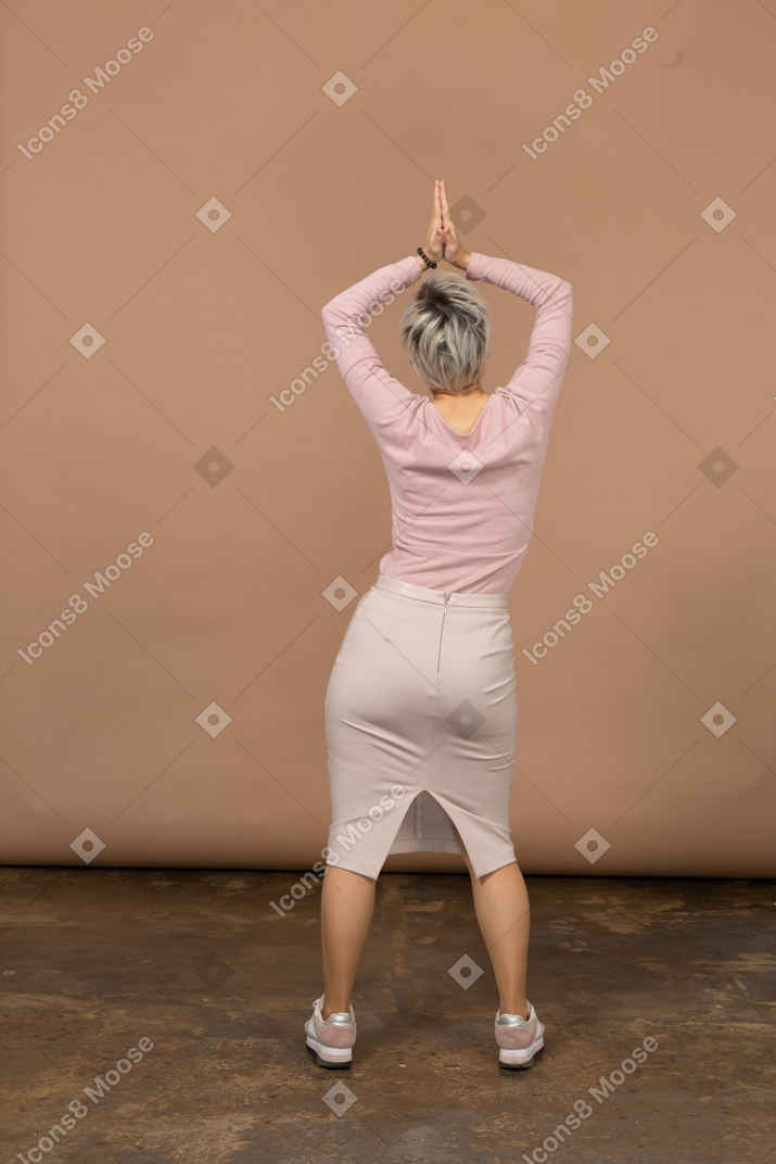 Vue arrière d'une femme en vêtements décontractés posant dos à la caméra avec les mains au-dessus de la tête