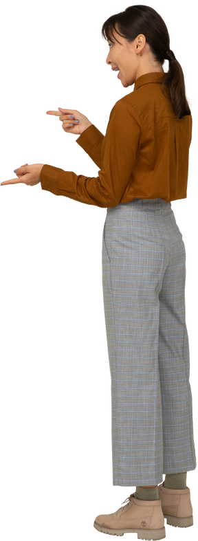 Vista posterior de tres cuartos de una mujer asiática joven emocional en calzones y blusa señalando con el dedo