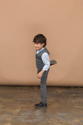 Side view of a boy in grey suit posing on one leg