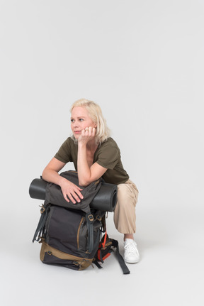 Pensive mature female tourist sitting near backpack