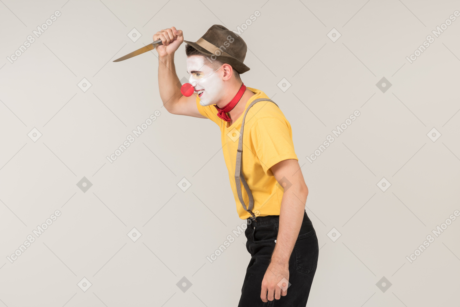 Male clown standing in profile and holding a knife